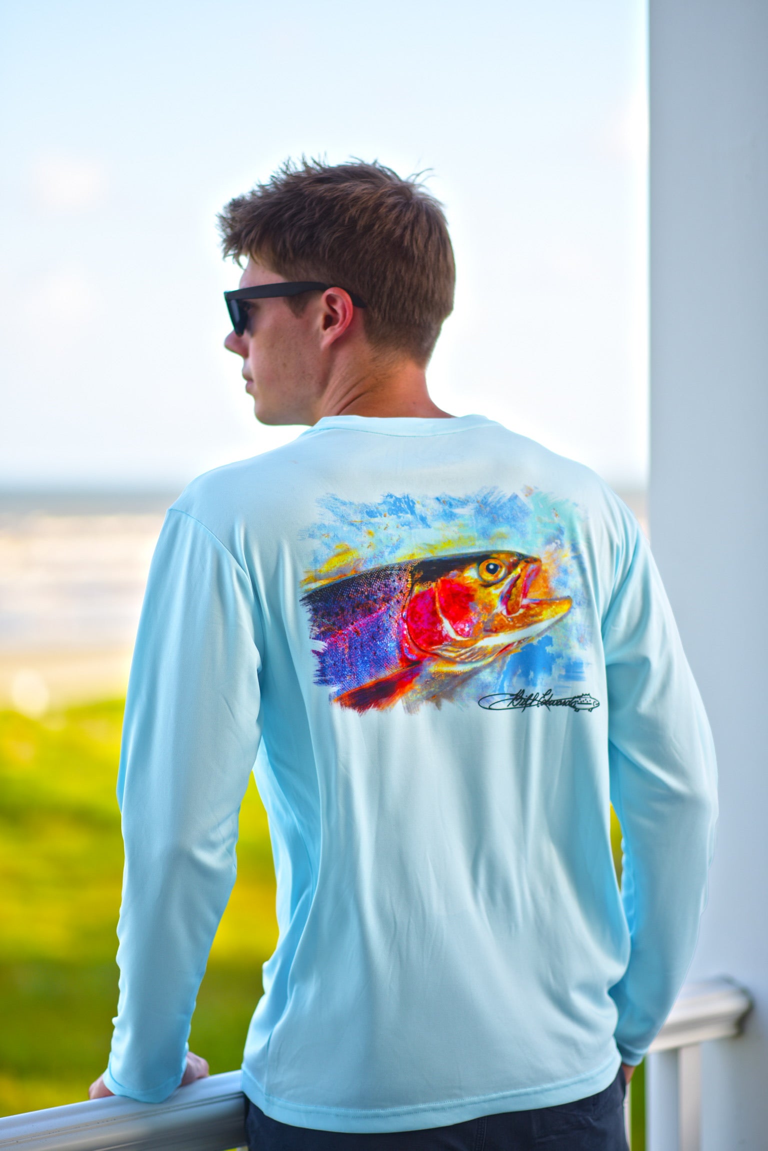 Man wearing Rainbow Trout UPF 50+ Shirt on a balcony, highlighting the artistic trout print and lightweight activewear fit.