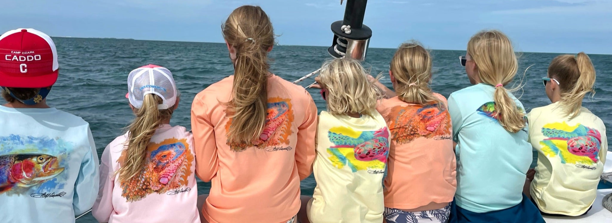 Group of kids wearing colorful Iguana Kids UPF 50+ Fishing Performance Shirts on a boat, showcasing vibrant iguana graphics and sun-safe long sleeves.