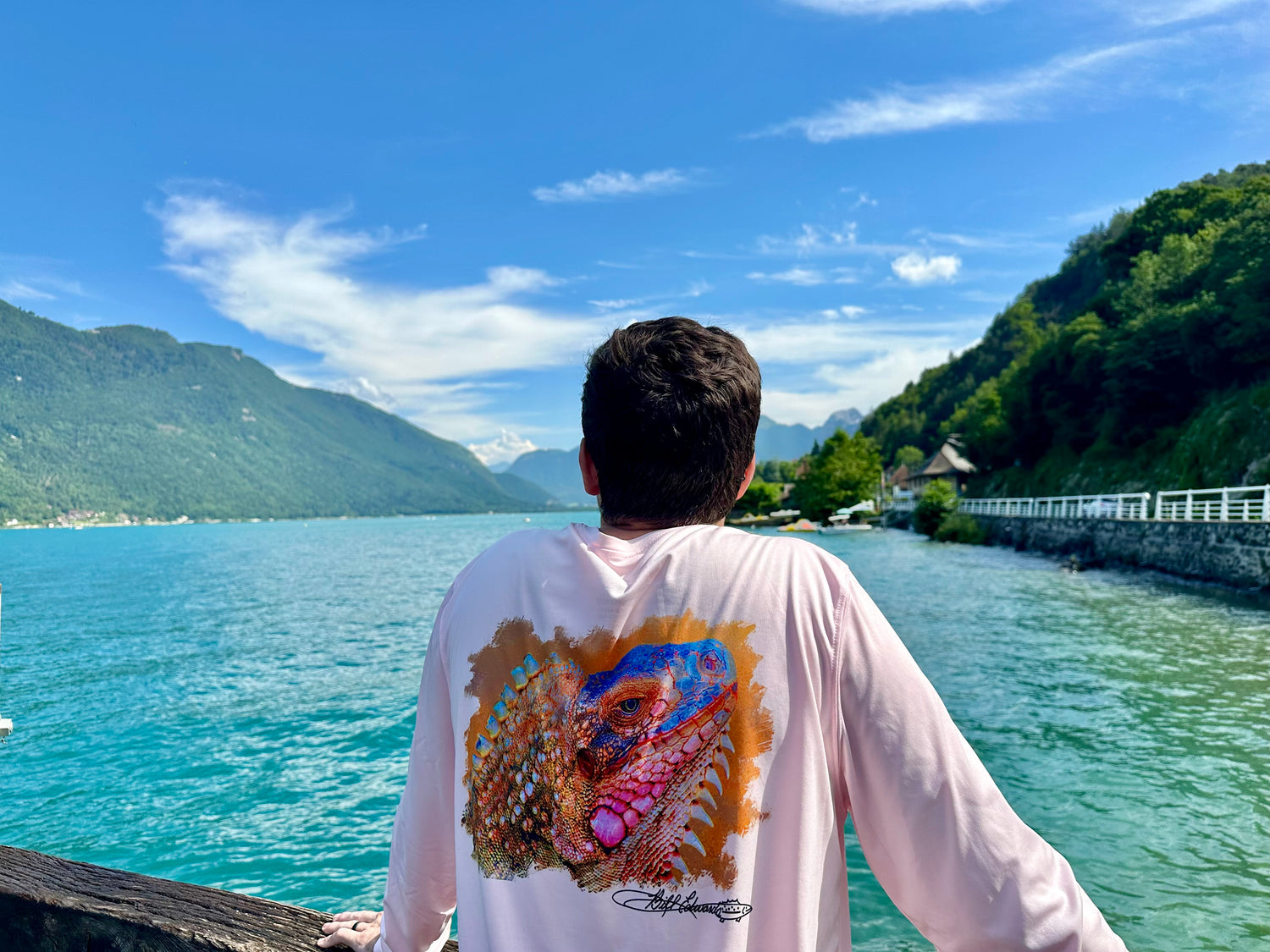 Man wearing Caribbean Iguana Performance Fishing Shirt - UPF 50+ with vibrant iguana artwork, standing by a scenic lake with mountains in the background.