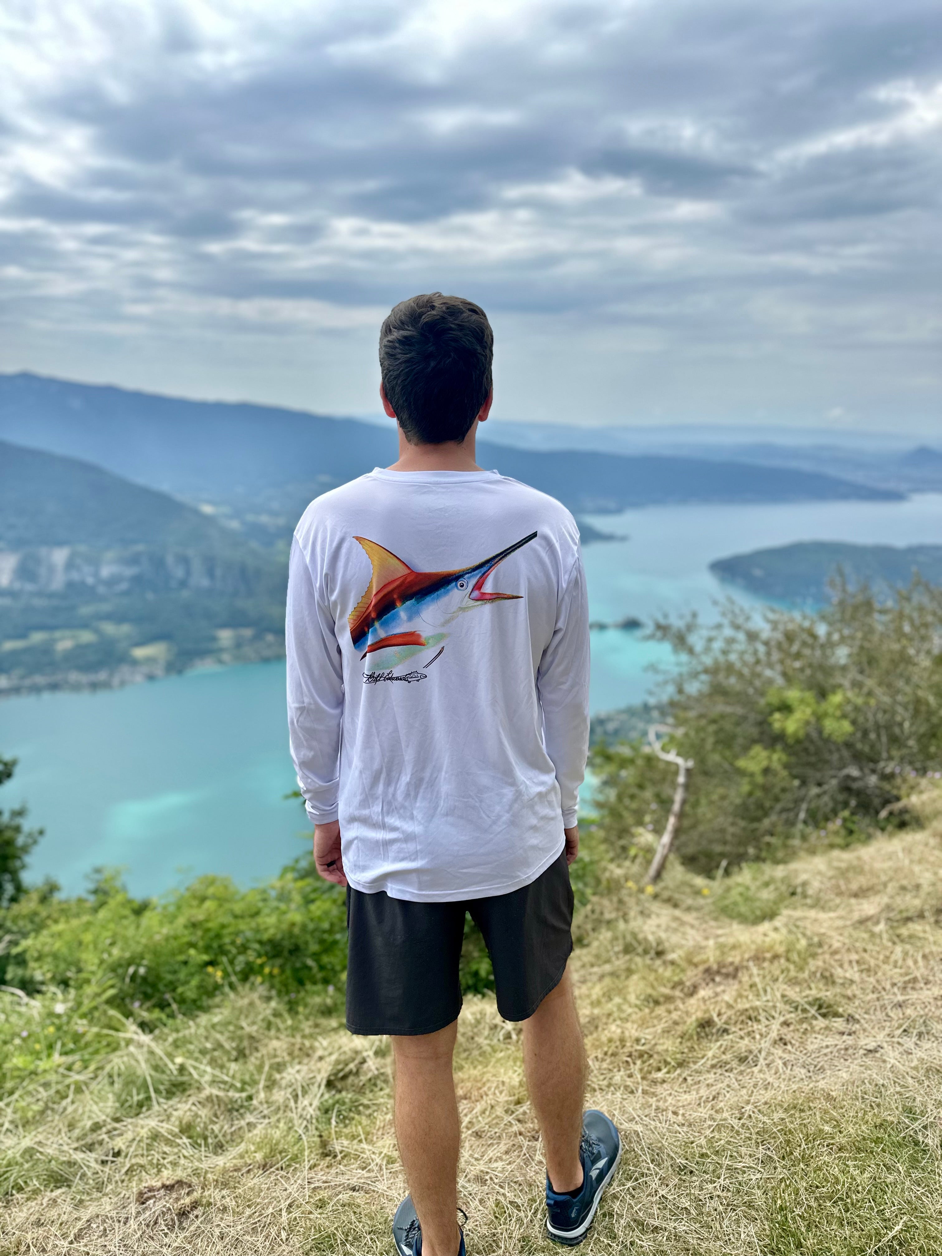 Man wearing Marlin Performance Fishing Shirt with UPF 50 sun protection, featuring colorful marlin artwork by Bill Edwards, overlooking a scenic lake view.