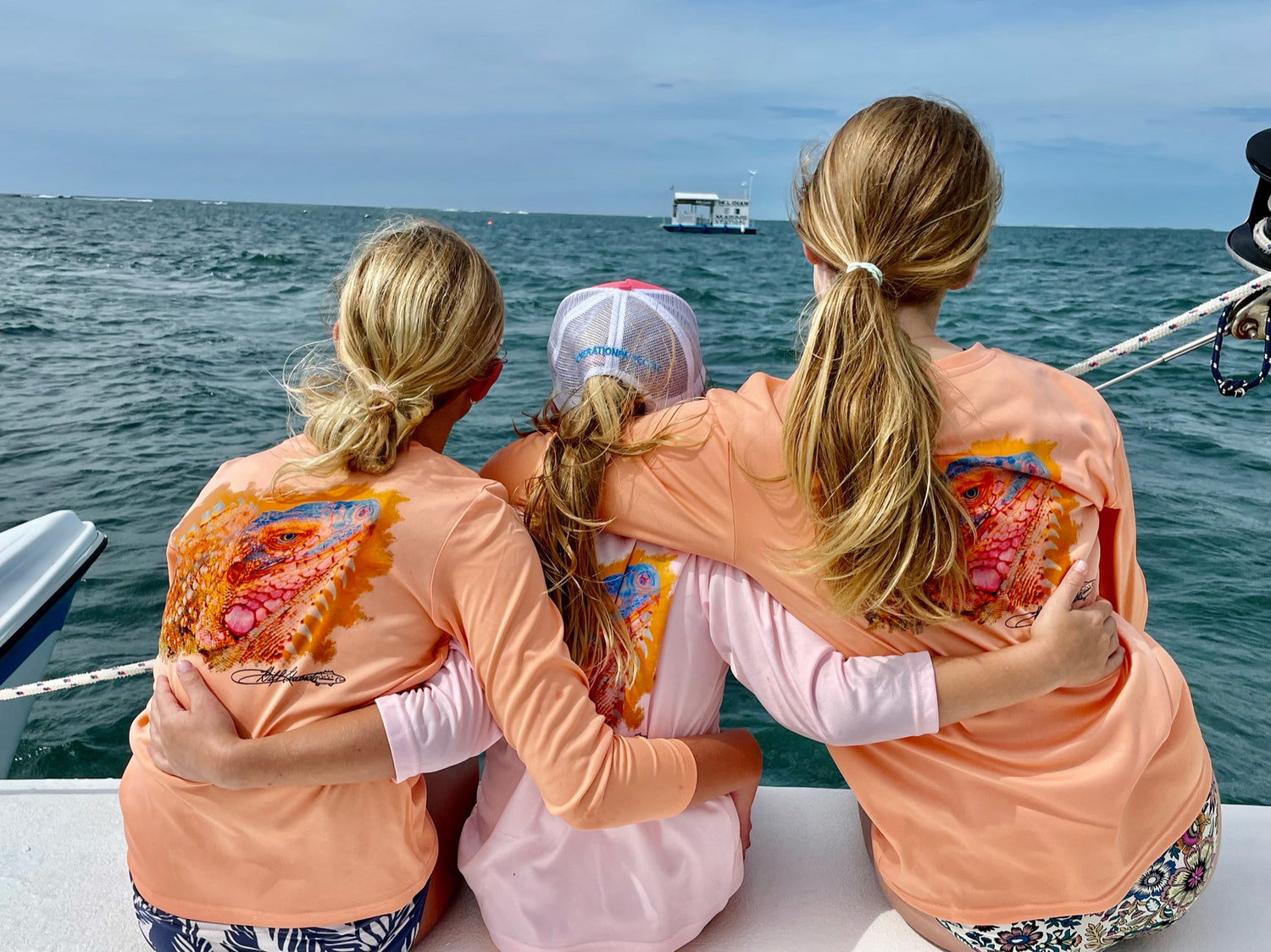Three girls on a boat wearing Iguana Kids UPF 50+ Fishing Performance Shirts in citrus orange and pink, designed for sun safety and moisture-wicking comfort.