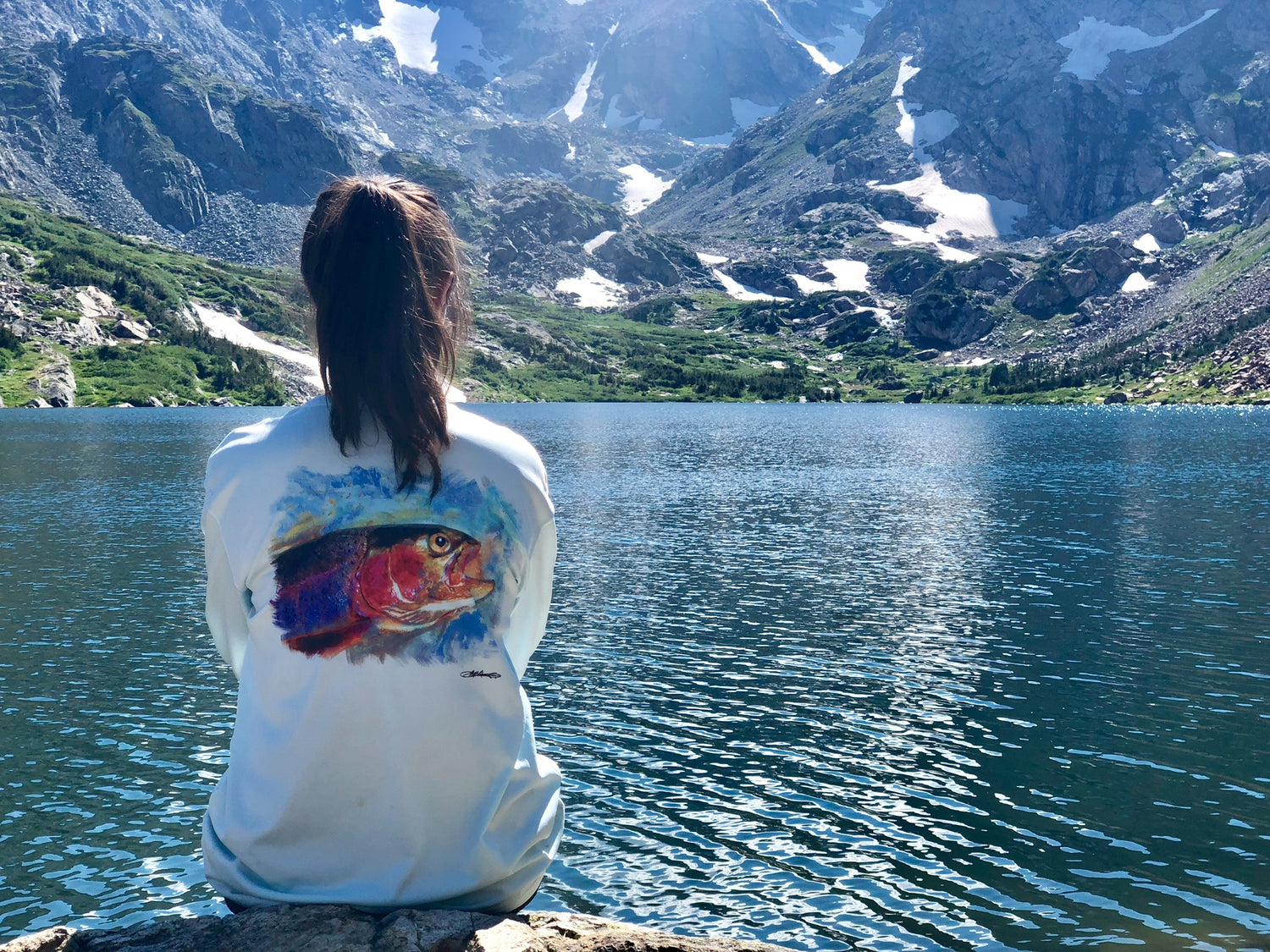 Woman sitting by alpine lake in Rainbow Trout UPF 50+ Shirt, featuring vibrant trout artwork and moisture-wicking comfort.