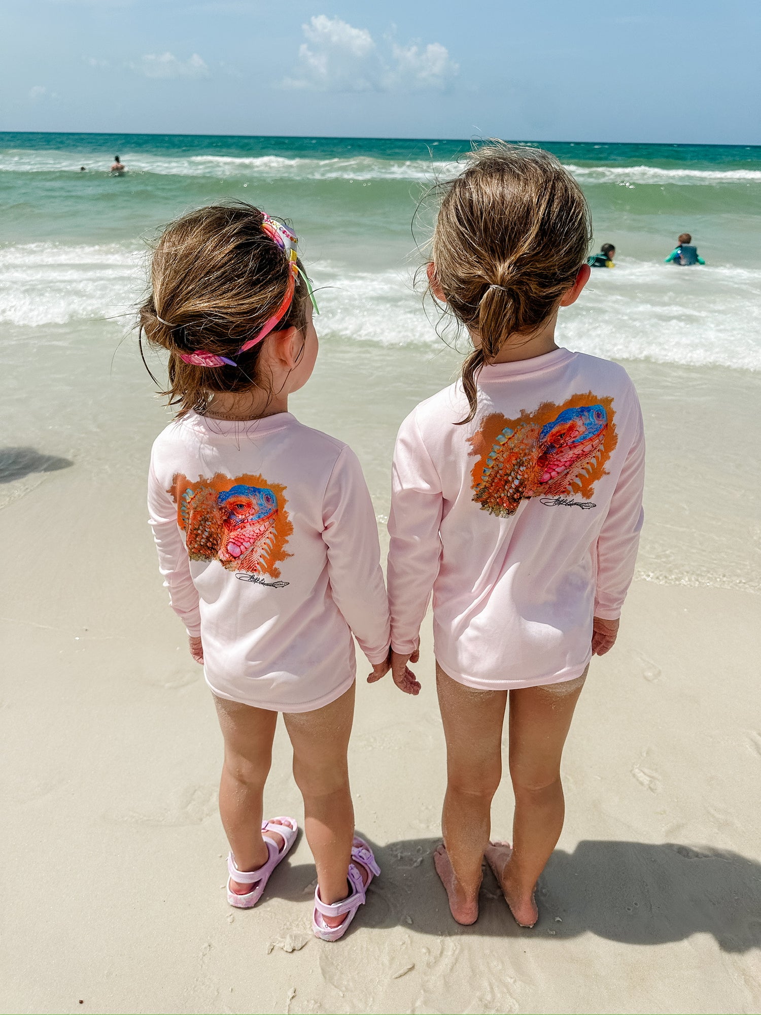Two kids at the beach wearing matching Caribbean Iguana Kids Performance Fishing Shirts UPF 50+ with iguana back print.