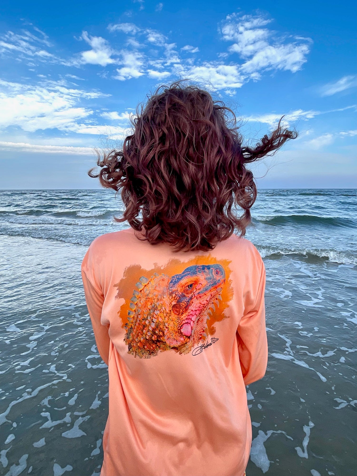 Child at the beach wearing citrus orange Iguana Kids UPF 50+ Fishing Performance Shirt with iguana design, ideal for sun protection and outdoor play.