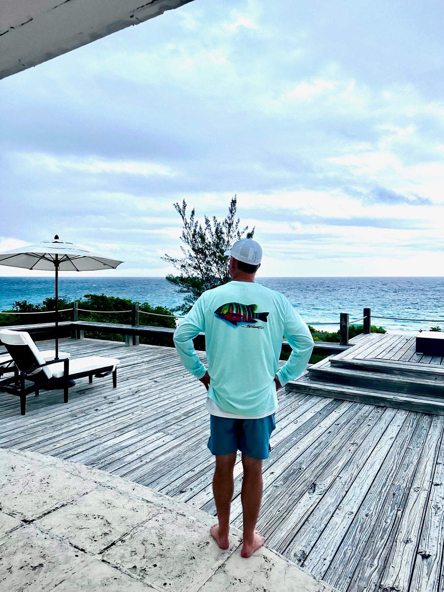 Man wearing Santiago Snapper Performance Fishing Shirt UPF 50+ Sun Protection Moisture-Wicking on oceanfront deck. Long sleeve shirt with colorful snapper graphic.