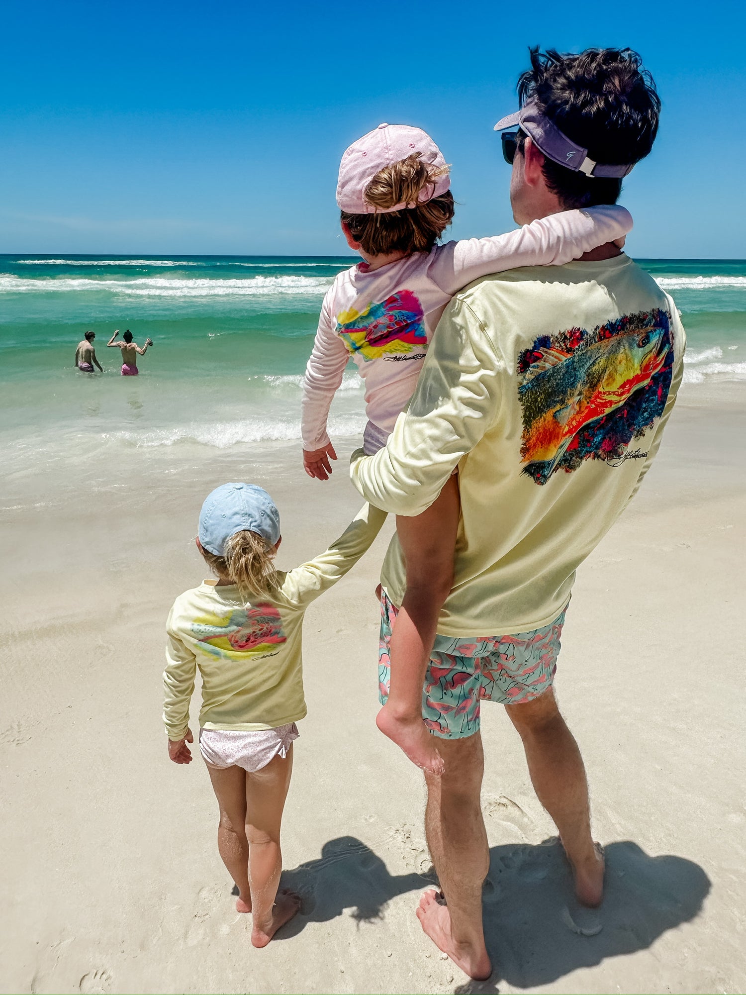 Father and daughters in matching Speckled Trout UPF 50+ Fishing Shirts at the beach, emphasizing family sun protection and stylish fishing apparel.