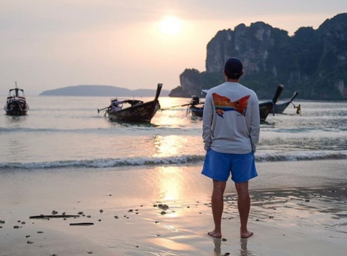 Man wearing Redfish Design Fishing Shirt with UPF 50 standing on beach at sunset. Long sleeve performance shirt ideal for sun protection and fishing.