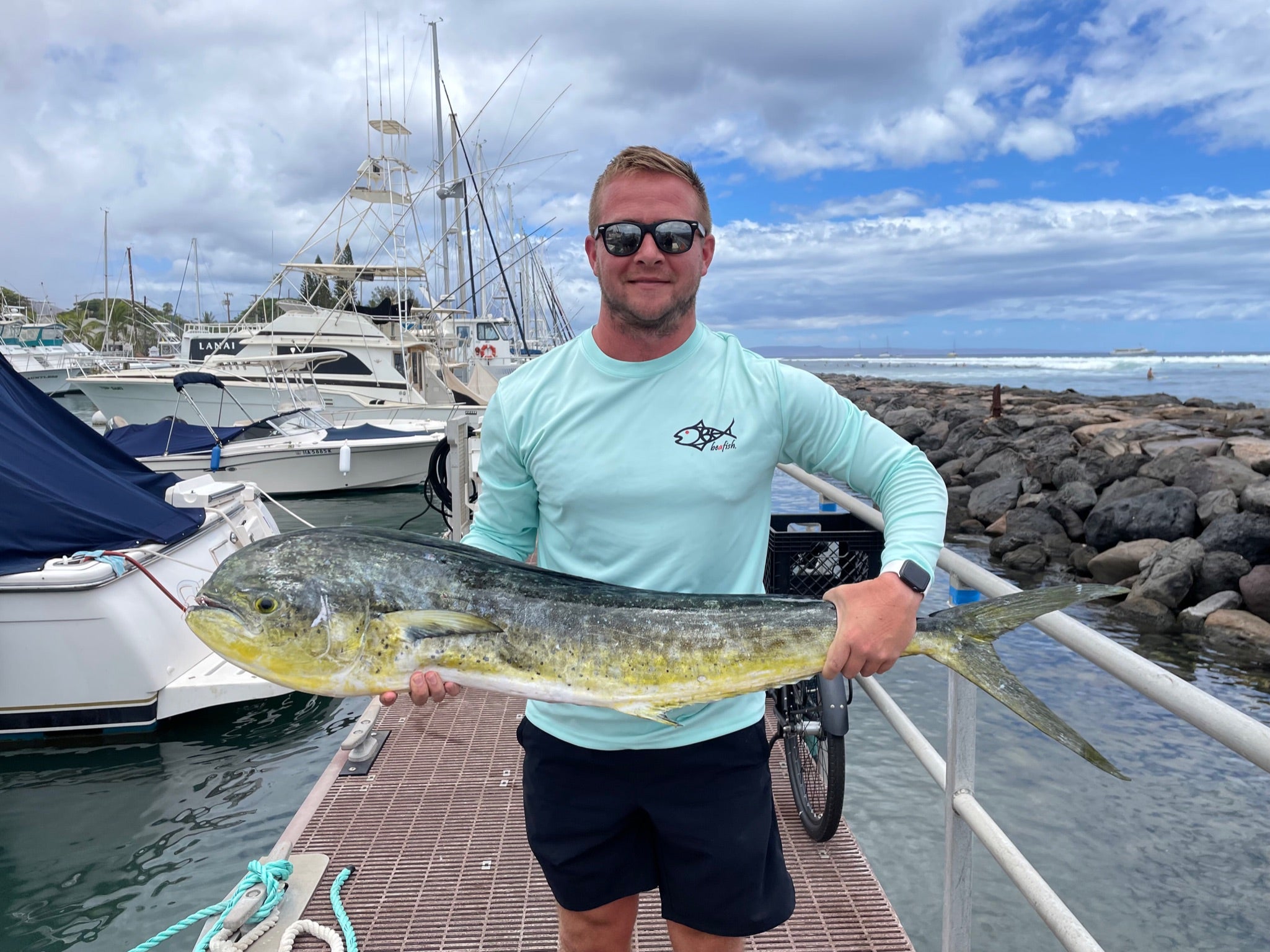 Man holding large fish at marina in Rainbow Trout UPF 50+ Shirt, showing front logo and ideal fit for fishing performance wear.