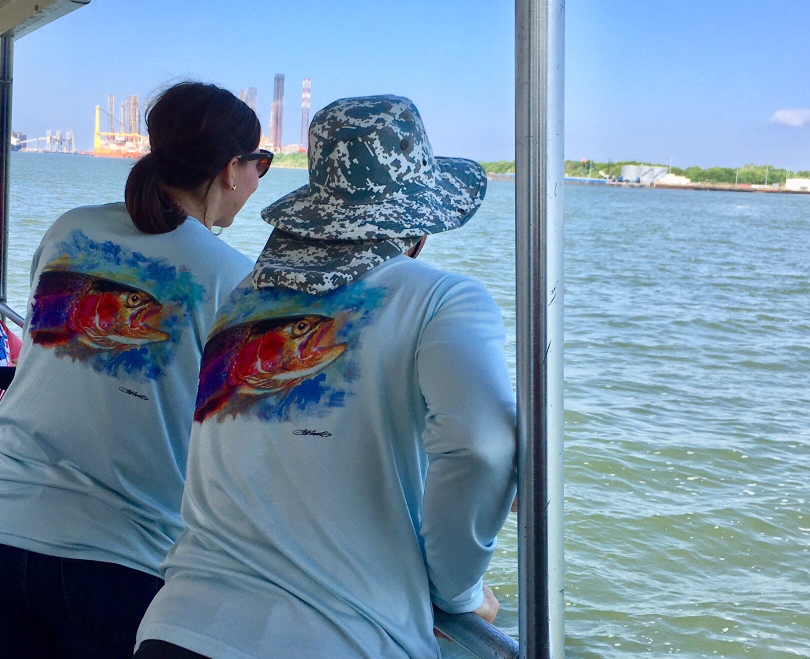 Two women wearing Rainbow Trout UPF 50+ Shirts on a boat, showcasing the colorful trout design ideal for sunny fishing trips.