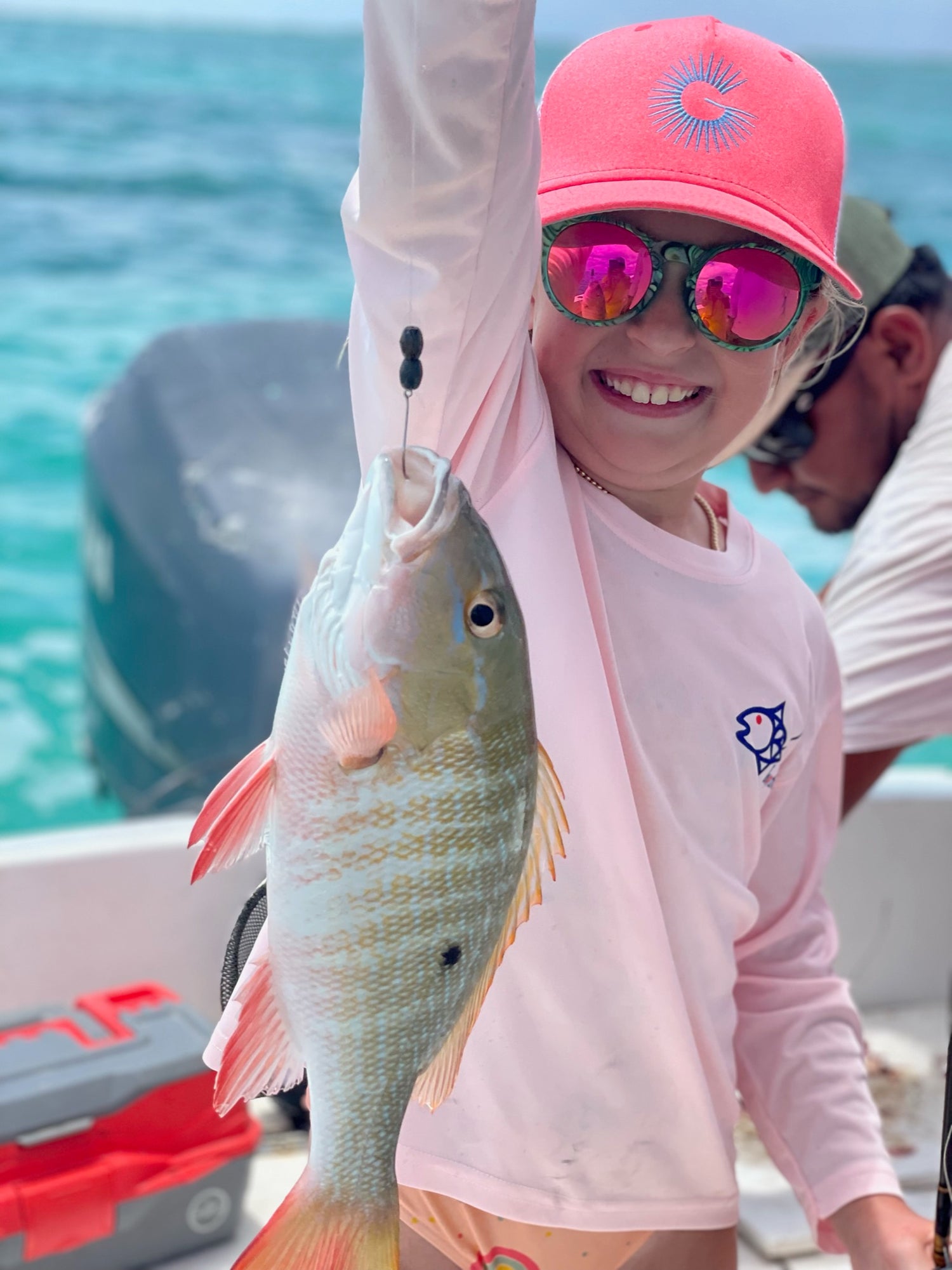Child wearing Caribbean Iguana Kids Performance Fishing Shirt UPF 50+ holding a fish on a boat, showcasing sun-protective activewear.