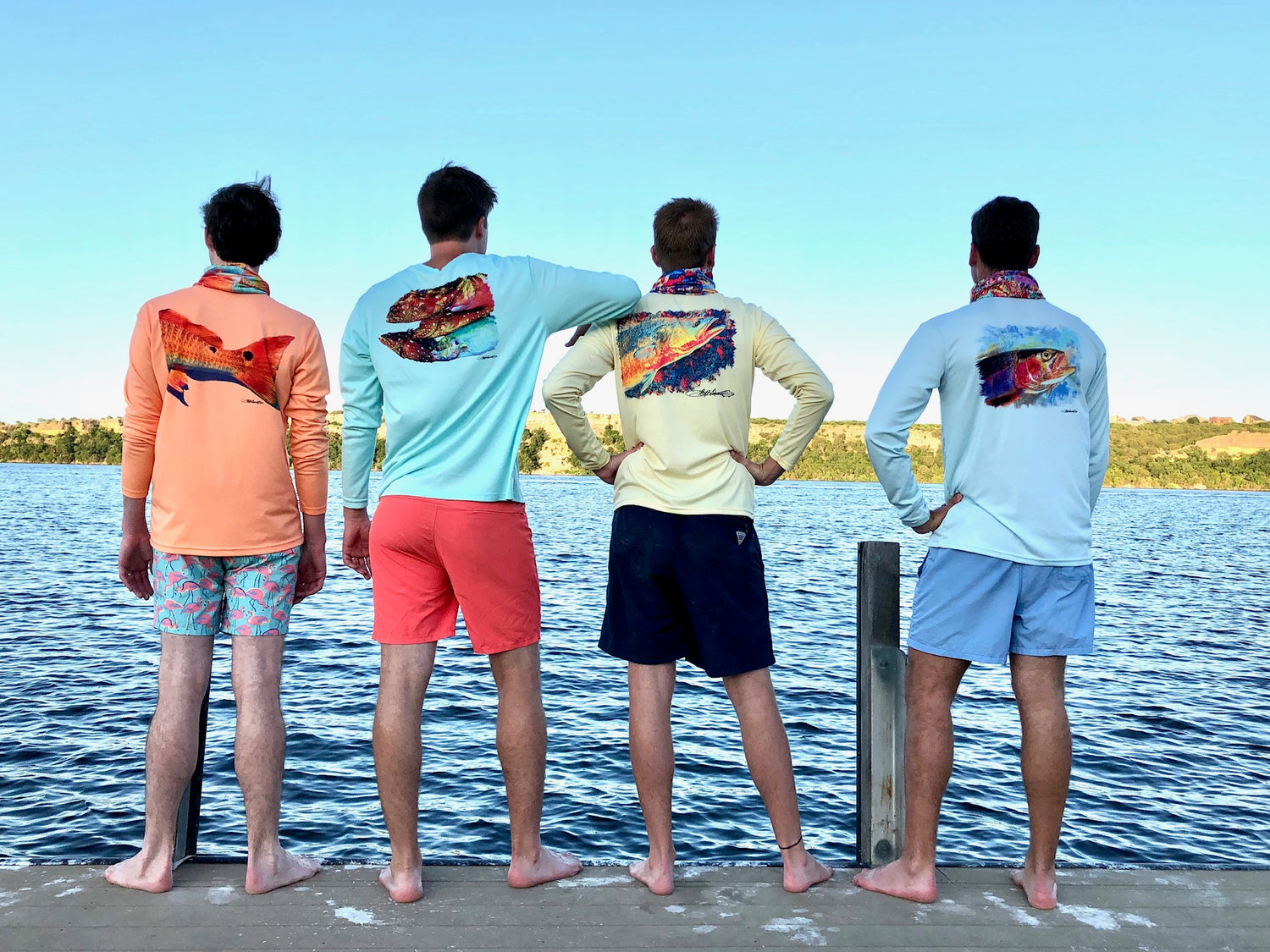 Group of men wearing various Speckled Trout UPF 50+ Fishing Shirts by the lake, showcasing colorful back designs and activewear versatility.