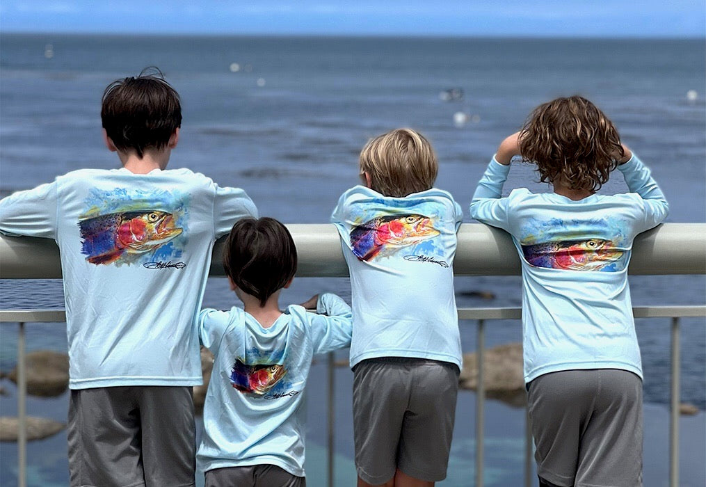 Group of kids wearing Rocky Rainbow Trout Kids Performance Fishing Shirts with trout artwork, enjoying ocean view in sun-protective activewear.