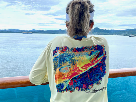 Woman wearing Speckled Trout UPF 50+ Fishing Shirt with colorful trout design while overlooking the ocean, showcasing sun-safe fishing apparel.