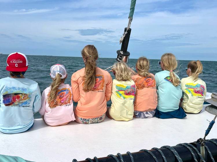 Kids wearing colorful BeAFish KIDS fishing sun protecting performance shirts sitting on a boat at sea. toddler and youth fishing shirt