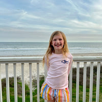 Smiling girl wearing Caribbean Iguana Kids Performance Fishing Shirt UPF 50+ with fish logo, standing on a beachside balcony.