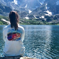 Woman sitting by alpine lake in Rainbow Trout UPF 50+ Shirt, featuring vibrant trout artwork and moisture-wicking comfort.