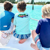 Three boys wearing Santiago Snapper Kids Performance Fishing Shirts UPF 50+ on a boat, showcasing colorful snapper design and beach-ready activewear.
