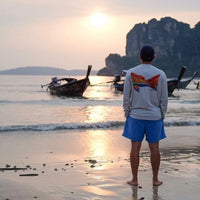 Man wearing Redfish Design Fishing Shirt with UPF 50 standing on beach at sunset. Long sleeve performance shirt ideal for sun protection and fishing.