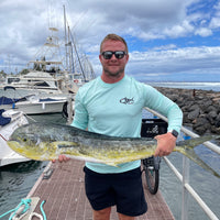 Man holding large fish at marina in Rainbow Trout UPF 50+ Shirt, showing front logo and ideal fit for fishing performance wear.