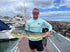 Man holding large fish at marina in Rainbow Trout UPF 50+ Shirt, showing front logo and ideal fit for fishing performance wear.