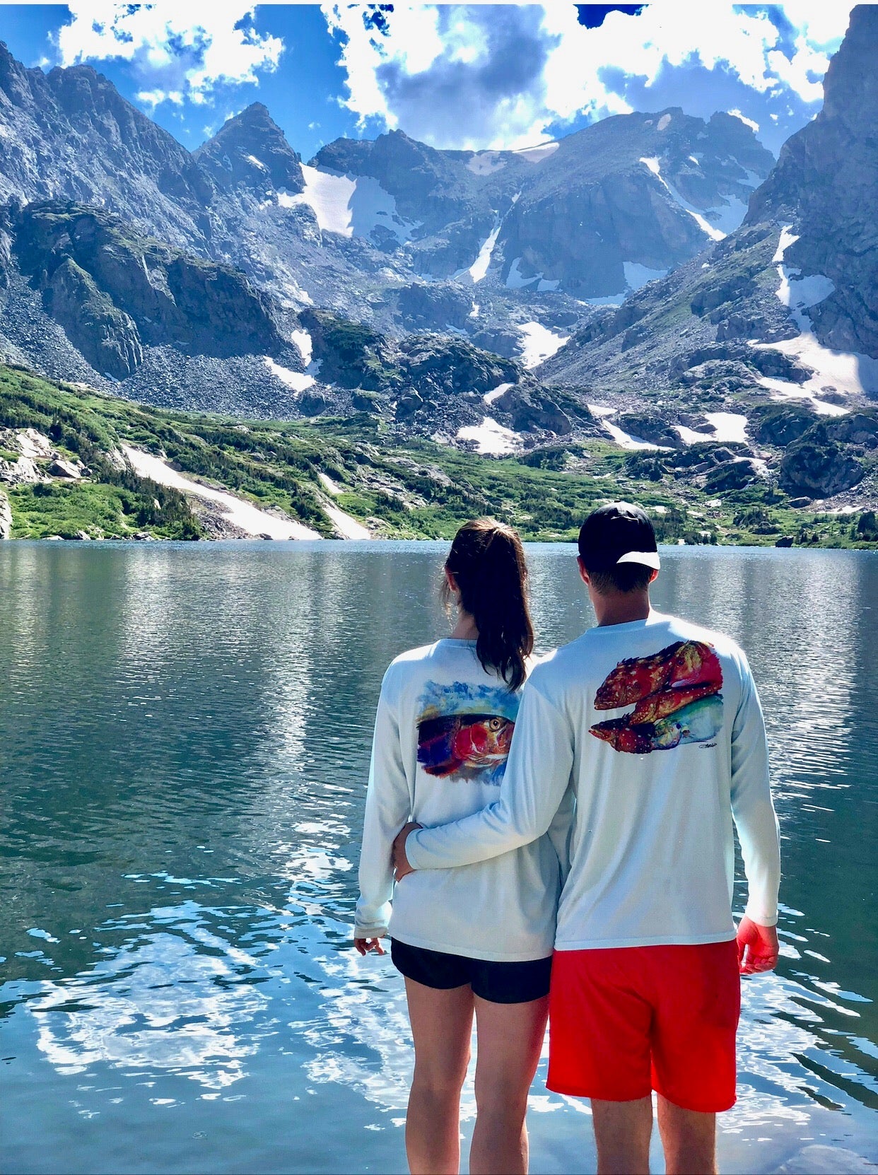 Couple wearing Rainbow Trout UPF 50+ Shirts by mountain lake, displaying matching trout artwork for outdoor couples' apparel.
