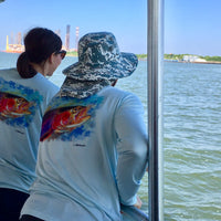 Two women wearing Rainbow Trout UPF 50+ Shirts on a boat, showcasing the colorful trout design ideal for sunny fishing trips.