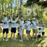 Group of men and children in matching Rainbow Trout UPF 50+ Shirts by a river, perfect for family fishing and outdoor adventures.