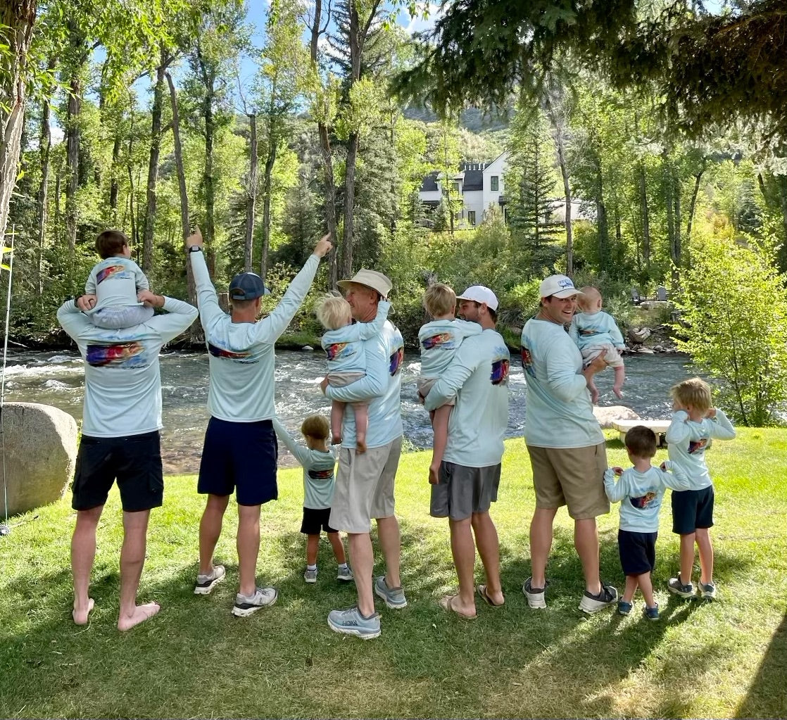 Group of men and children in matching Rainbow Trout UPF 50+ Shirts by a river, perfect for family fishing and outdoor adventures.