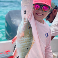 Child wearing Caribbean Iguana Kids Performance Fishing Shirt UPF 50+ holding a fish on a boat, showcasing sun-protective activewear.