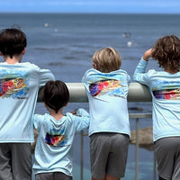 Group of kids wearing Rocky Rainbow Trout Kids Performance Fishing Shirts with trout artwork, enjoying ocean view in sun-protective activewear.