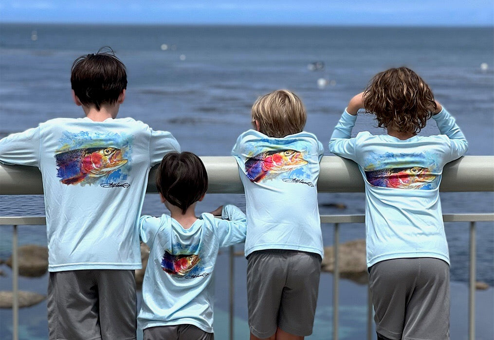 Group of kids wearing Rocky Rainbow Trout Kids Performance Fishing Shirts with trout artwork, enjoying ocean view in sun-protective activewear.