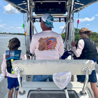 Man wearing Caribbean Iguana Performance Fishing Shirt - UPF 50+ with original iguana artwork on back, fishing on a boat with two kids.