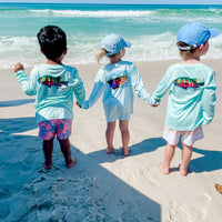 Kids holding hands on the beach wearing Santiago Snapper Performance Fishing Shirts UPF 50+, featuring colorful snapper art and sun-protective fabric.